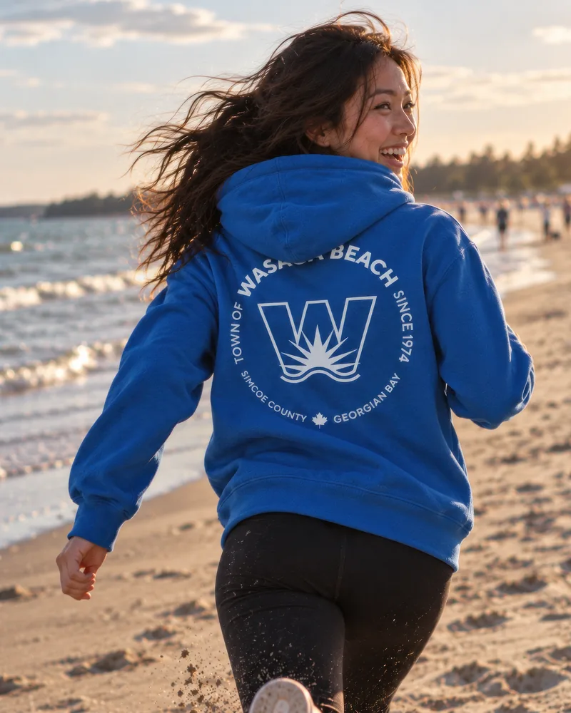 The Midweight Hoodie in royal with the town crest on the back, worn on Wasaga Beach